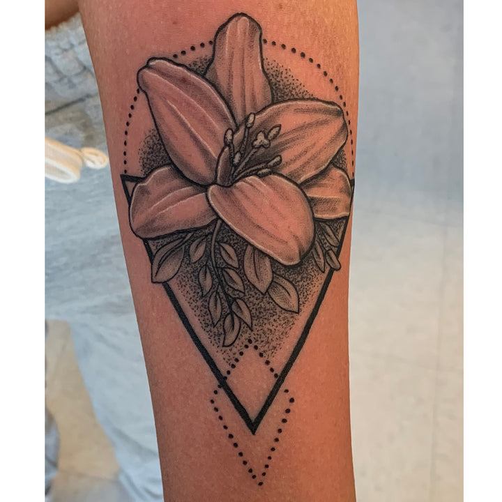 Black and grey lilly tattoo surrounded by a simple geometric design and pepper shading in the backgroumd.
