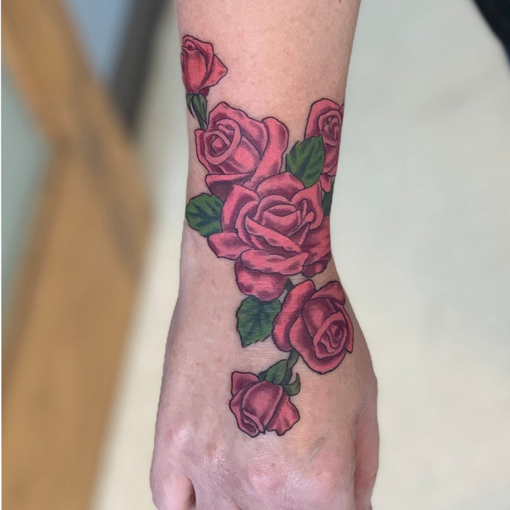 Pink roses with a few green leaves on the outer wrist and hand of a woman.