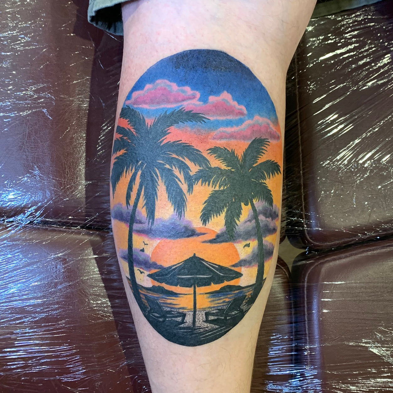 color tattoo of sunset at the beach on the back of a calf