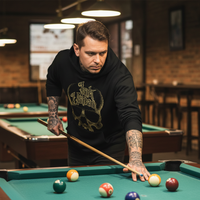 Black & Gold Dot Work Skull Hoodie — Tattooed male model wearing black Ink Union Tattoo Co. black and gold dot work skull hoodie leaning over pool table mid-shot — alternative streetwear, tattoo artist sweatshirt, unisex heavy blend hoodie, edgy cool fashion