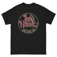 A black t-shirt with a gold circle containing fancy lettering in red and gold that says Ink Union and a gold tattoo machine peeking out from behind on the right side.  There is a dot work gradient inside the circle, and the words Tattoo Co. in gold are at the bottom of the design.
