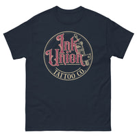 A navy blue t-shirt with a gold circle containing fancy lettering in red and gold that says Ink Union and a gold tattoo machine peeking out from behind on the right side.  There is a dot work gradient inside the circle, and the words Tattoo Co. in gold are at the bottom of the design.
