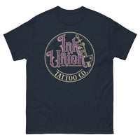 A navy blue t-shirt with a gold circle containing fancy lettering in purple and gold that says Ink Union and a gold tattoo machine peeking out from behind on the right side.  There is a dot work gradient inside the circle, and the words Tattoo Co. in gold are at the bottom of the design.
