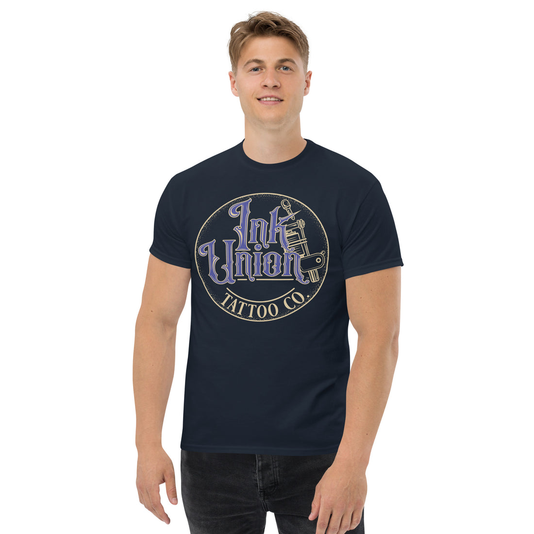 An attractive man wearing a black t-shirt with a gold circle containing fancy lettering in blue and gold that says Ink Union and a gold tattoo machine peeking out from behind on the right side.  There is a dot work gradient inside the circle, and the words Tattoo Co. in gold are at the bottom of the design.