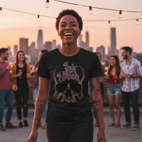 Purple & Gold Dot Work Skull Tee — Tattooed Native American male model wearing black Ink Union Tattoo Co. purple and gold dot work skull graphic tee at outdoor farmers market with colorful vendor tents and green trees in background — alternative streetwear, tattoo artist t-shirt, unisex graphic tee, edgy cool fashion