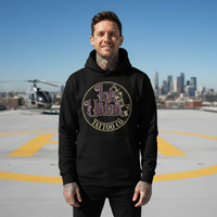 Purple & Gold Flash Art Hoodie — Tattooed male model wearing black Ink Union Tattoo Co. purple and gold flash art tattoo machine hoodie on rooftop helipad with helicopter in background — alternative streetwear, tattoo artist sweatshirt, unisex heavy blend hoodie, edgy cool fashion