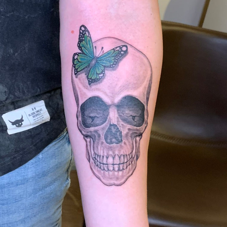black and grey realistic skull with a green butterfly hovering over the forehead