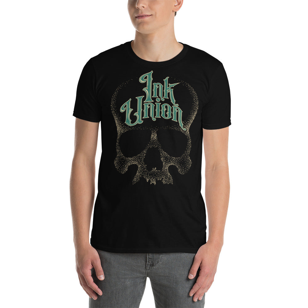 An attractive man wearing a black t-shirt  adorned with a gold dot work human skull and the words Ink Union in fancy gold and green lettering across the forehead of the skull.