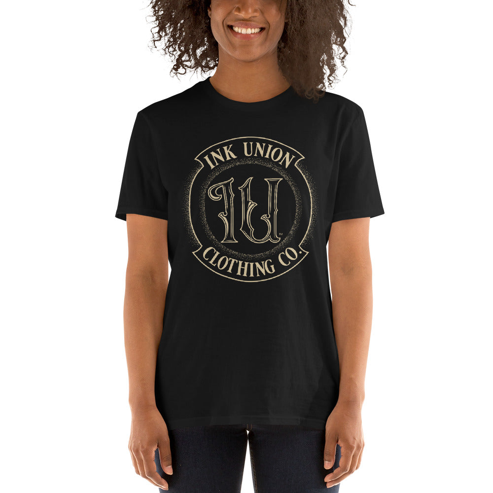 An attractive woman is wearing a black t-shirt adorned with the Ink Union Clothing Co gold badge logo containing fancy lettering and dot work gradients.