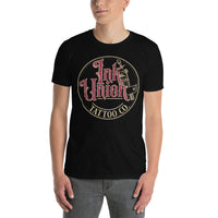 An attractive man wearing a black t-shirt with a gold circle containing fancy lettering in red and gold that says Ink Union and a gold tattoo machine peeking out from behind on the right side.  There is a dot work gradient inside the circle, and the words Tattoo Co. in gold are at the bottom of the design.