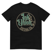 A black t-shirt with a gold circle containing fancy lettering in green and gold that says Ink Union and a gold tattoo machine peeking out from behind on the right side.  There is a dot work gradient inside the circle, and the words Tattoo Co. in gold are at the bottom of the design.