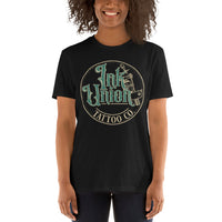An attractive woman wearing a black t-shirt with a gold circle containing fancy lettering in green and gold that says Ink Union and a gold tattoo machine peeking out from behind on the right side.  There is a dot work gradient inside the circle, and the words Tattoo Co. in gold are at the bottom of the design.