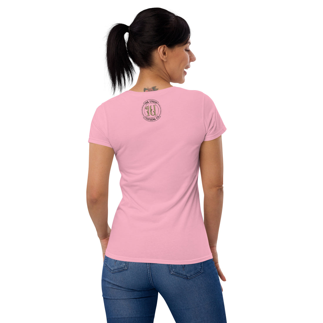 The rear view of an attractive woman wearing a pink t-shirt with a small gold and black Ink Union badge logo centered just under the neckline.