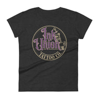A dark grey t-shirt with a gold circle containing fancy lettering in purple and gold that says Ink Union and a gold tattoo machine peeking out from behind on the right side. There is a dot work gradient inside the circle, and the words Tattoo Co. in gold are at the bottom of the design.