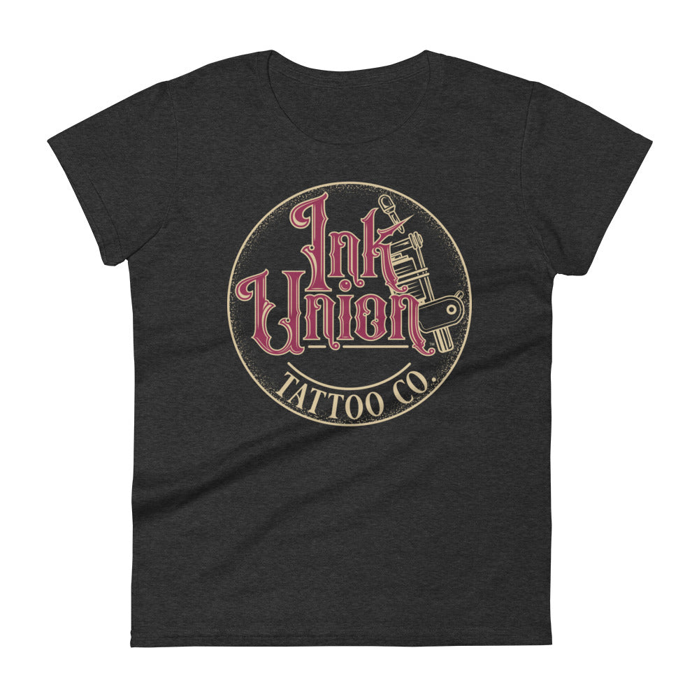 A dark grey t-shirt with a gold circle containing fancy lettering in red and gold that says Ink Union and a gold tattoo machine peeking out from behind on the right side. There is a dot work gradient inside the circle, and the words Tattoo Co. in gold are at the bottom of the design.