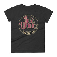 A dark grey t-shirt with a gold circle containing fancy lettering in red and gold that says Ink Union and a gold tattoo machine peeking out from behind on the right side. There is a dot work gradient inside the circle, and the words Tattoo Co. in gold are at the bottom of the design.