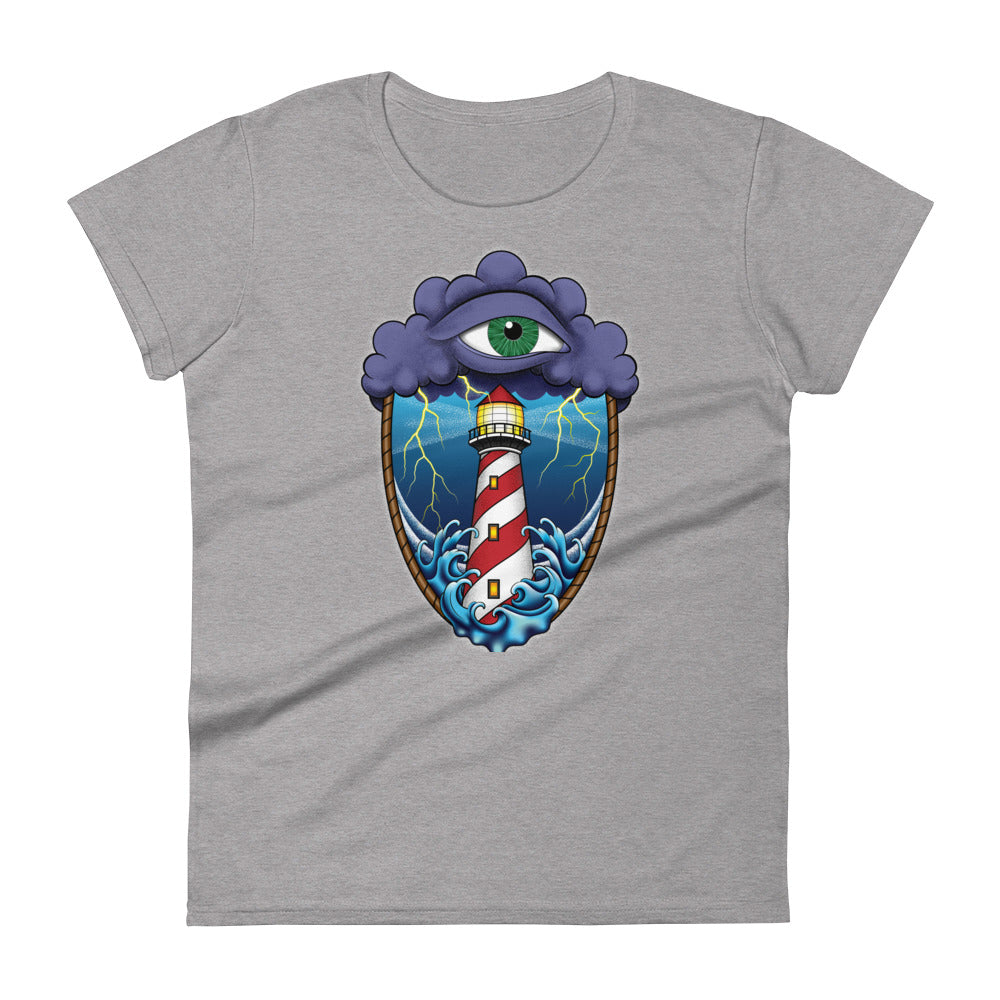 A light grey t-shirt with an old school eye of the storm tattoo design of large dark purple storm clouds at the top of the design with a green eye in the middle of the clouds.  Below the clouds is an oval shape with brown rope. Inside the rope are stormy seas and a lighthouse with lightning striking in the background.  At the bottom of the design, some of the waves are spilling out of the rope barrier. The sky and seas are hues of blue; the lighthouse is white and red striped like a barber pole.