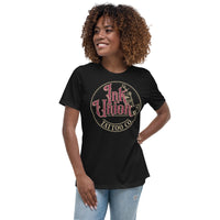An attractive woman wearing a black t-shirt with a gold circle containing fancy lettering in red and gold that says Ink Union and a gold tattoo machine peeking out from behind on the right side.  There is a dot work gradient inside the circle, and the words Tattoo Co. in gold are at the bottom of the design.