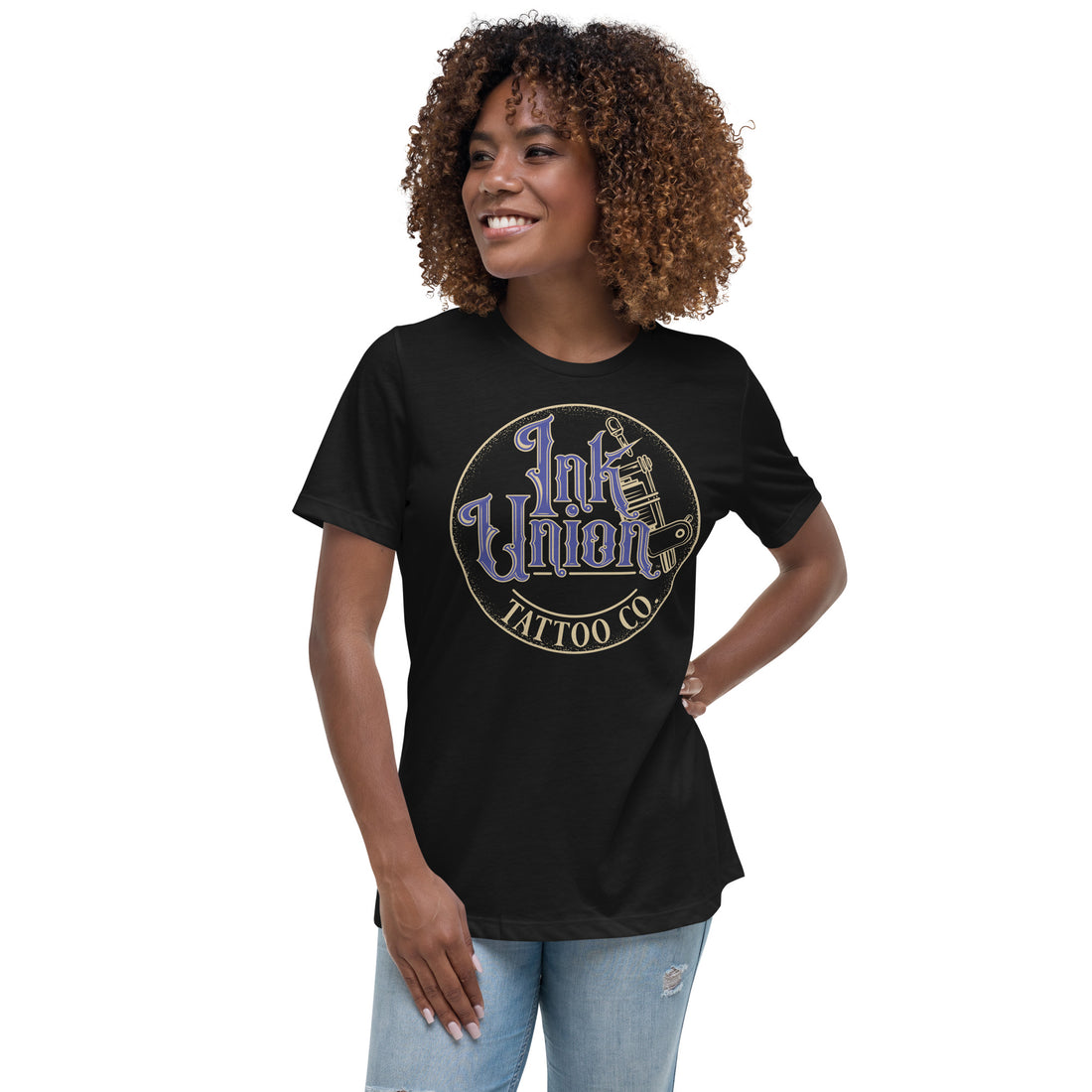 An attractive woman wearing a black t-shirt with a gold circle containing fancy lettering in blue and gold that says Ink Union and a gold tattoo machine peeking out from behind on the right side.  There is a dot work gradient inside the circle, and the words Tattoo Co. in gold are at the bottom of the design.
