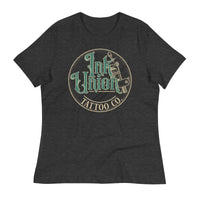 A dark grey t-shirt with a gold circle containing fancy lettering in green and gold that says Ink Union and a gold tattoo machine peeking out from behind on the right side. There is a dot work gradient inside the circle, and the words Tattoo Co. in gold are at the bottom of the design.