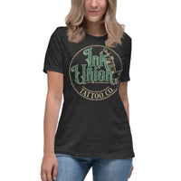 An attractive woman wearing a dark grey t-shirt with a gold circle containing fancy lettering in green and gold that says Ink Union and a gold tattoo machine peeking out from behind on the right side.  There is a dot work gradient inside the circle, and the words Tattoo Co. in gold are at the bottom of the design.