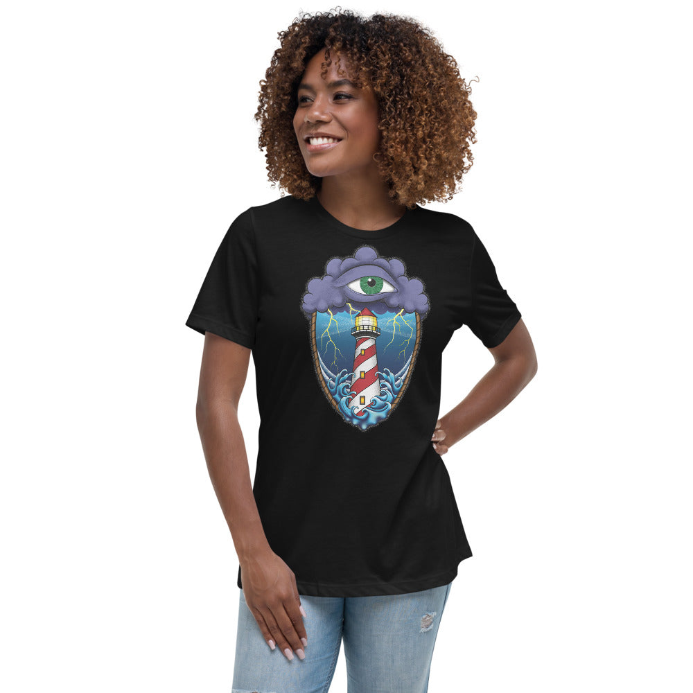 An attractive woman wearing a black t-shirt with an old school eye of the storm tattoo design of large dark purple storm clouds at the top of the design with a green eye in the middle of the clouds.  Below the clouds is an oval shape with brown rope. Inside the rope are stormy seas and lightning striking at a lighthouse that is white and red striped like a barber pole.
