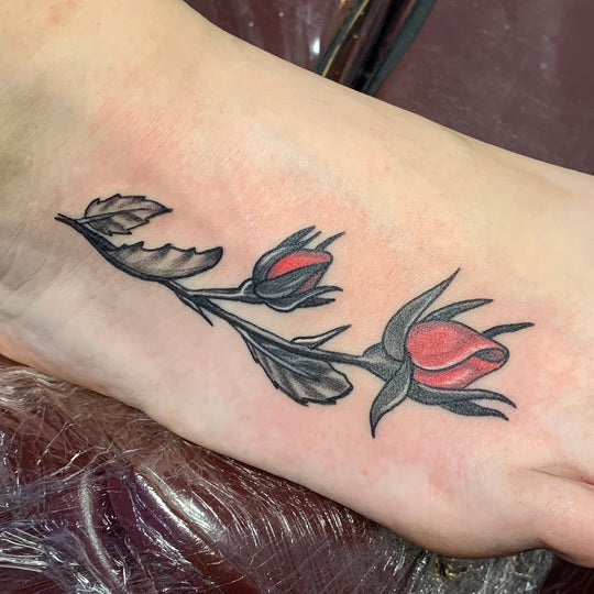 Black and red rose tattoo on the outside of a woman's foot.