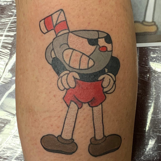 Tattoo of the game character Cuphead in the back of a thigh.