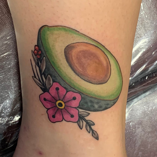 Neo-traditional style tattoo of half an avocado with a pink flower.