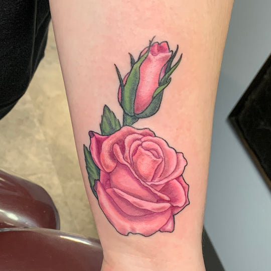 A pink rose with a bud tattoo on the inside of a womans wrist.
