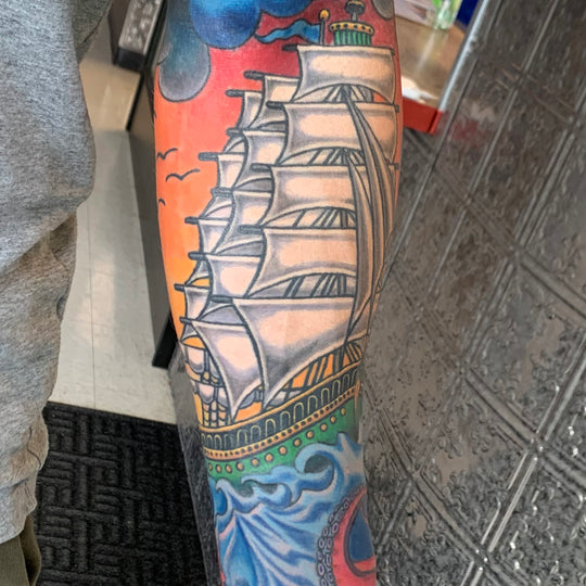 A traditional style clipper ship tattoo on a mans lower arm.