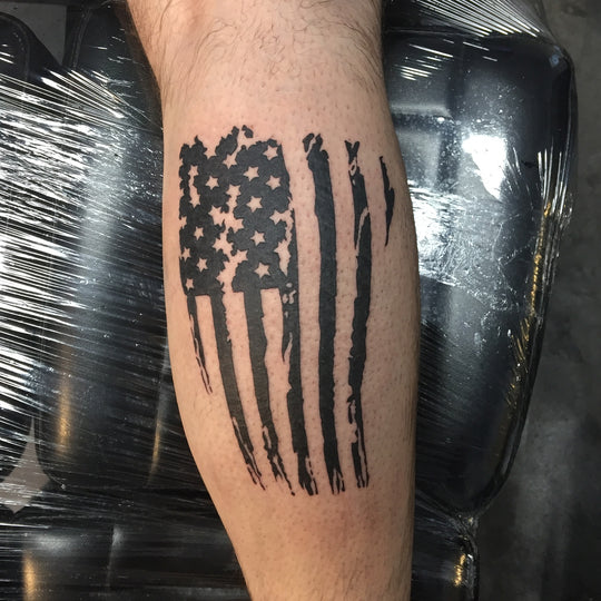 Tattoo of a torn american flag in black on the back of a mans calf.