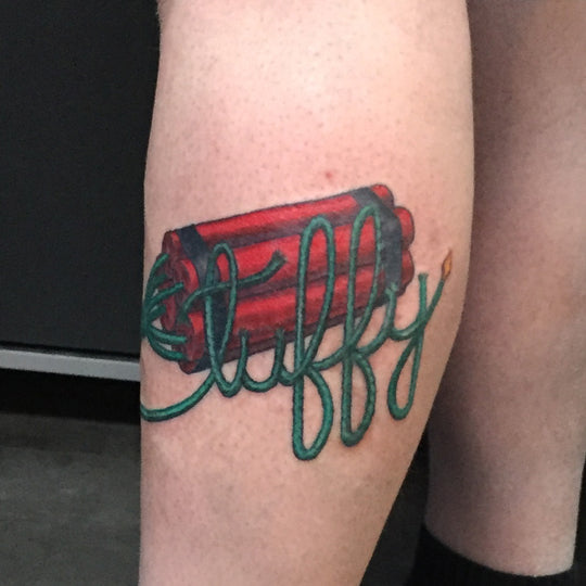 A color tattoo of dynamite with a long green fuse forming the name tuffy.