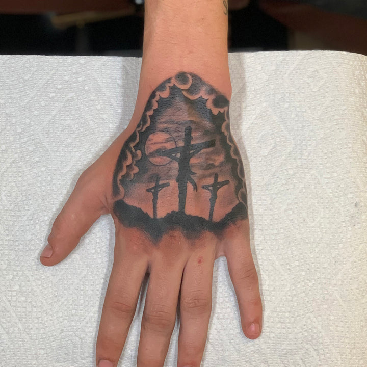 black and grey hand tattoo of the three crosses surrounded by storm clouds at sunset
