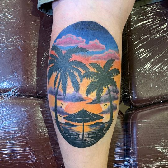 color tattoo of sunset at the beach on the back of a calf