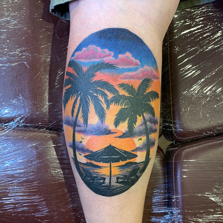 color tattoo of sunset at the beach on the back of a calf