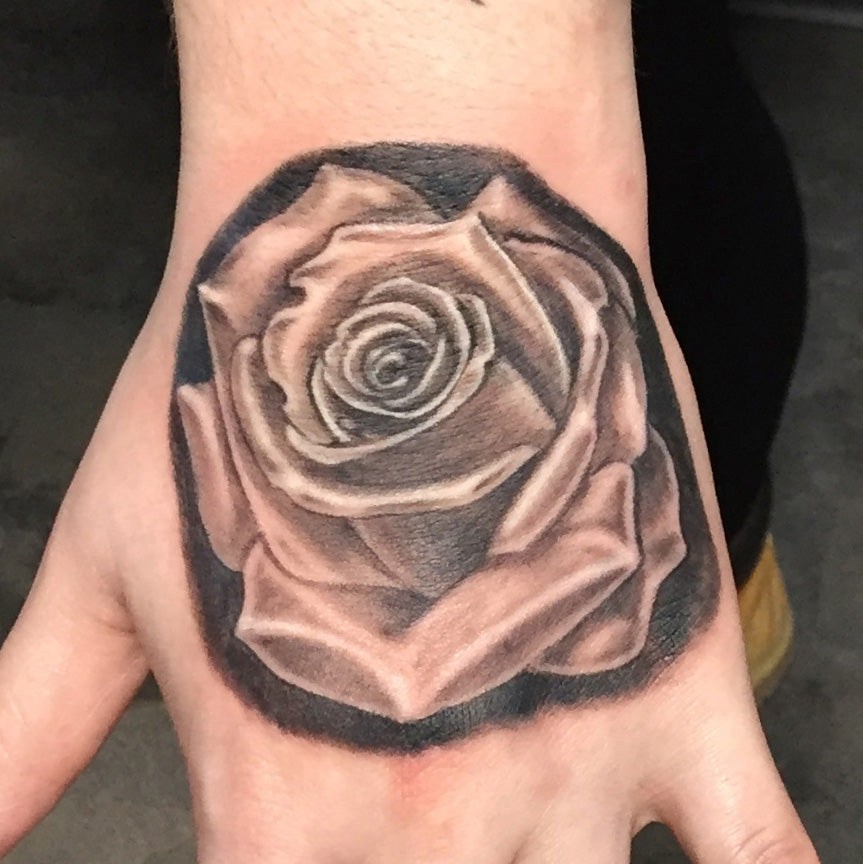 realisitc black and grey tattoo of a rose on the top of a hand