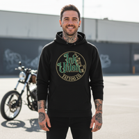 Green & Gold Flash Art Hoodie — Tattooed male model wearing black Ink Union Tattoo Co. green and gold flash art tattoo machine hoodie with custom chopper motorcycle in background — alternative streetwear, tattoo artist sweatshirt, unisex heavy blend hoodie, edgy cool fashion

