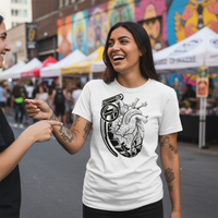 Heart Attack Vol. 2 Tee — Tattooed Latina female model wearing white Ink Union heart attack anatomical heart grenade bold art unisex graphic tee laughing with friend at outdoor street art fair with colorful murals and vendor tents in background — alternative streetwear, tattoo artist t-shirt, unisex graphic tee, bold dark art fashion