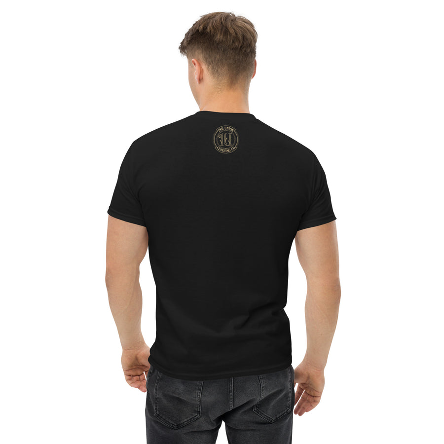 The back view of an attractive man wearing a black t-shirt with a small gold Ink Union Badge Logo centered just under the neckline.