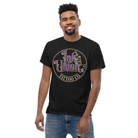 An attractive man wearing a black t-shirt with a gold circle containing fancy lettering in purple and gold that says Ink Union and a gold tattoo machine peeking out from behind on the right side.  There is a dot work gradient inside the circle, and the words Tattoo Co. in gold are at the bottom of the design.