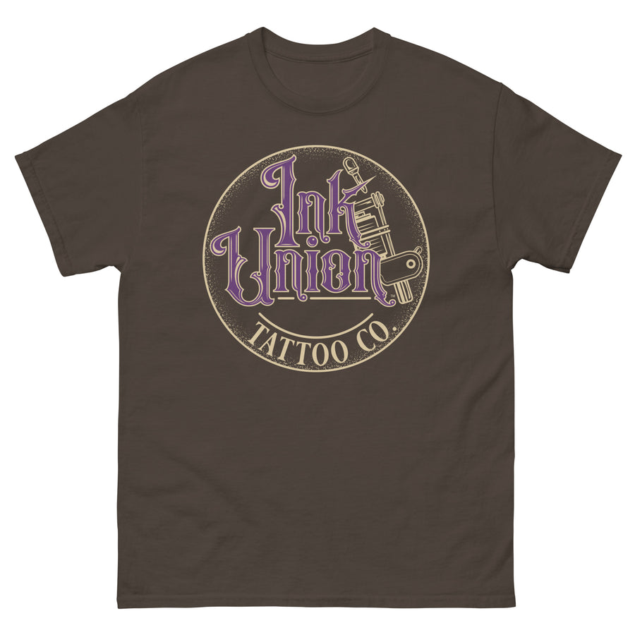 A dark brown t-shirt with a gold circle containing fancy lettering in purple and gold that says Ink Union and a gold tattoo machine peeking out from behind on the right side.  There is a dot work gradient inside the circle, and the words Tattoo Co. in gold are at the bottom of the design.