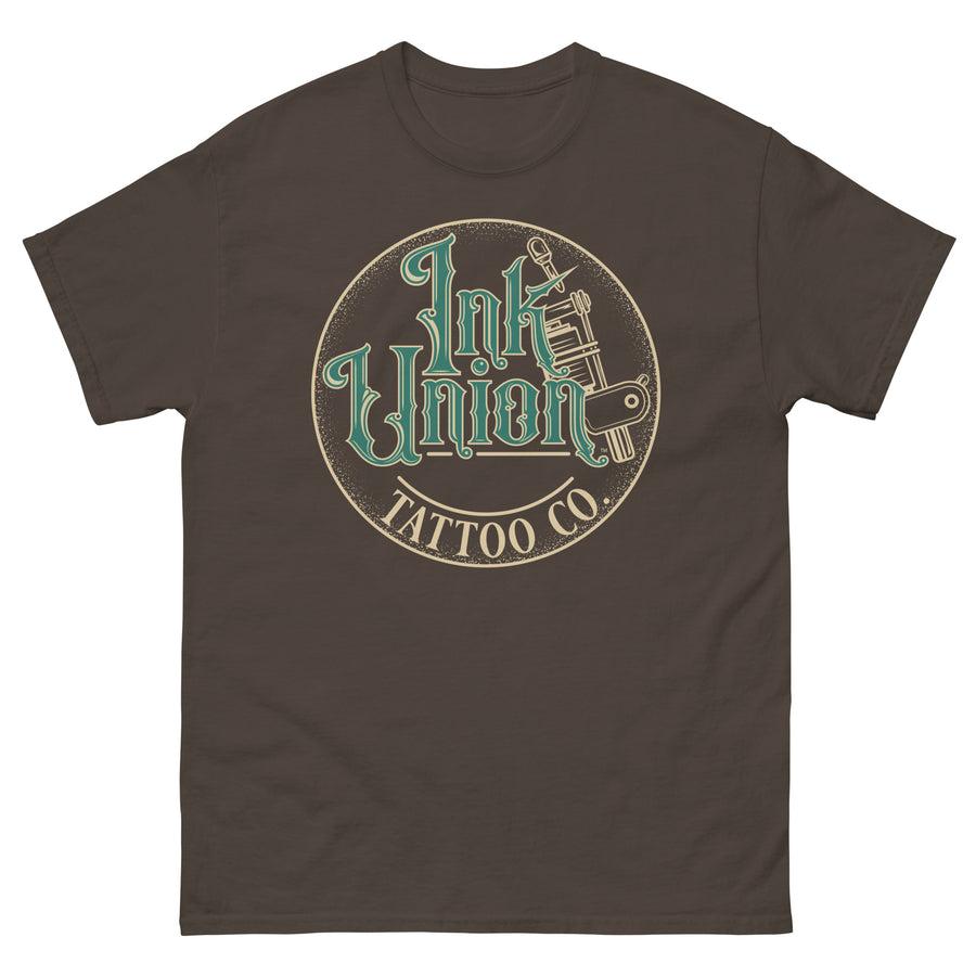 A dark brown t-shirt with a gold circle containing fancy lettering in green and gold that says Ink Union and a gold tattoo machine peeking out from behind on the right side.  There is a dot work gradient inside the circle, and the words Tattoo Co. in gold are at the bottom of the design.
