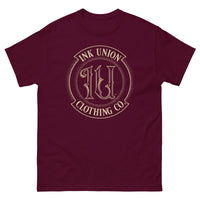 A maroon t-shirt adorned with the Ink Union Clothing Co gold badge logo containing fancy lettering and dot work gradients.