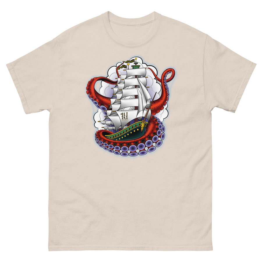 A sand color t-shirt with an old-school clipper ship tattoo design in green and brown with white sails surrounded by octopus tentacles in shades of red with purple tentacles. Behind the ship are purple-tinged clouds.