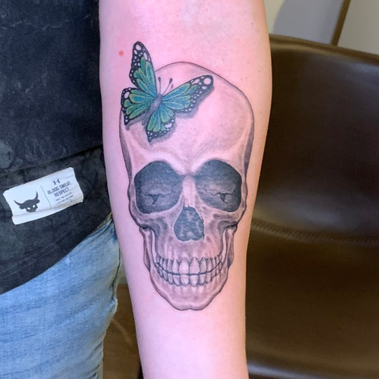 black and grey realistic skull with a green butterfly hovering over the forehead