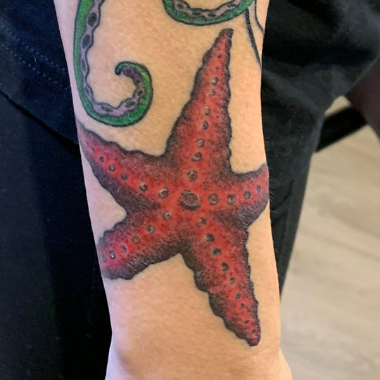 realistic red starfish tattoo located on the outside of a wrist