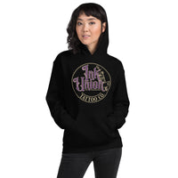 An attractive woman wearing a black hoodie with a gold circle containing fancy lettering in purple and gold that says Ink Union and a gold tattoo machine peeking out from behind on the right side.  There is a dot work gradient inside the circle, and the words Tattoo Co. in gold are at the bottom of the design.