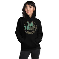 An attractive woman wearing a black hoodie with a gold circle containing fancy lettering in green and gold that says Ink Union and a gold tattoo machine peeking out from behind on the right side.  There is a dot work gradient inside the circle, and the words Tattoo Co. in gold are at the bottom of the design.