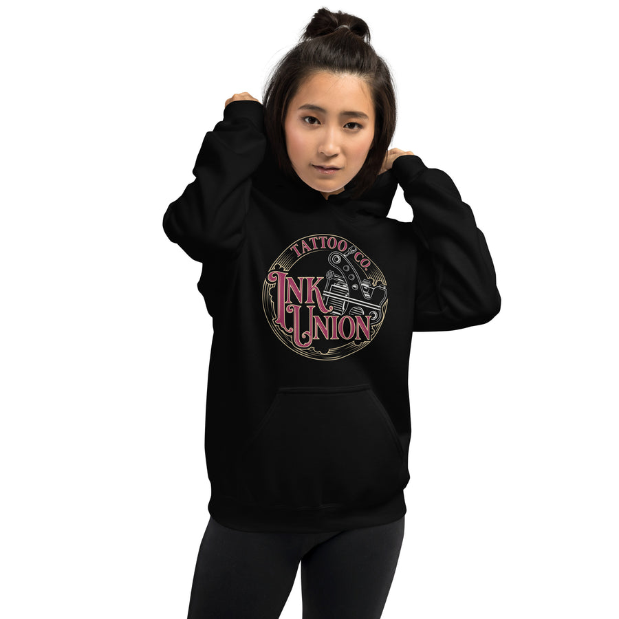 An attractive woman wearing a black hoodie  adorned with the Ink Union Tattoo Co. red and gold with a silver tattoo machine logo.